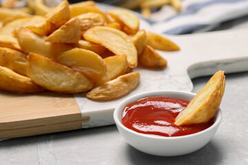 Delicious baked potato wedges and ketchup in bowl on light gray table, closeup