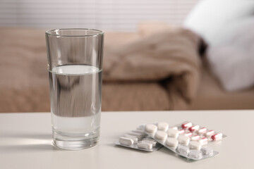 Glass of water and different pills in blisters on white table indoors, space for text