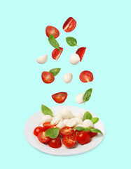 Fresh tomatoes. mozzarella cheese and basil leaves falling onto plate with Caprese salad against light blue background