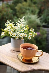 Cup of delicious chamomile tea and fresh flowers outdoors