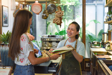 Young Vietnamese waitress working with check out machine and customers in cafe 