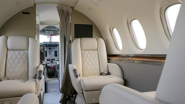 Luxurious passenger cabin of private corporate airplane with cozy white comfortable recliners. Bright salon with round portholes and open access to pilots cockpit