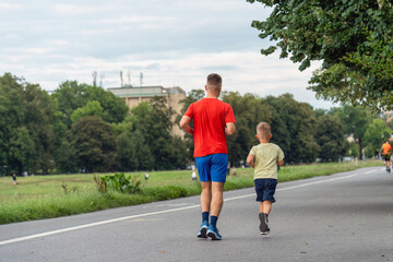 Obraz premium A happy father and his son enjoy a summer evening run in the park. They are smiling and having fun together. This is a perfect image for Father's Day, family, health and fitness concepts.