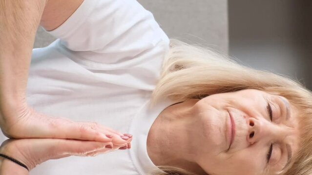 Portrait of an elderly fair-haired woman doing yoga. Meditation. Vertical video
