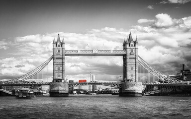 An iconic red London bus highlighted in a black and white image as it passes over Tower Bridge on...