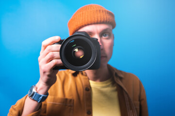 Happy smiling photographer taking pictures checking his camera settings in a studio shooting as content creator in blue background 