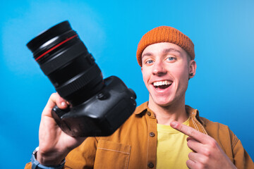Happy smiling young  photographer taking pictures checking his camera settings in a studio shooting as content creator in blue background 