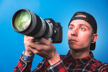Happy smiling photographer taking pictures checking his camera settings in a studio shooting as content creator in blue background 