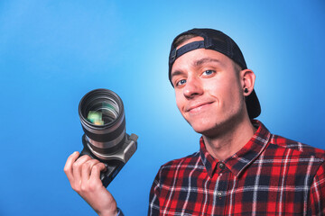 Happy smiling photographer taking pictures checking his camera settings in a studio shooting as content creator in blue background 