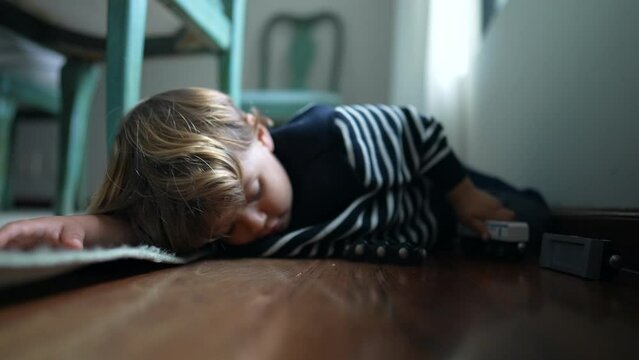 Child playing by himself on floor at home, one little boy engaged with his own imaginative world holding car toy in hand, laid on hardwood floor
