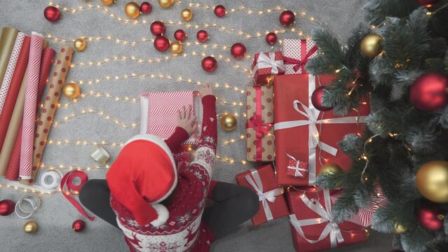 Inside the Christmas atmosphere, a woman pretends to wrap each box, creating gifts full of love and tenderness. Under the Christmas tree mouth, a woman diligently wraps gifts using paper that hides