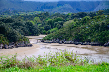 View on Playa de Poo during low tide near Llanes, Green coast of Asturias, North Spain with sandy beaches, cliffs, hidden caves, green fields and mountains.