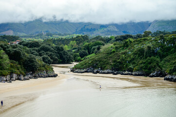 View on Playa de Poo during low tide near Llanes, Green coast of Asturias, North Spain with sandy beaches, cliffs, hidden caves, green fields and mountains.