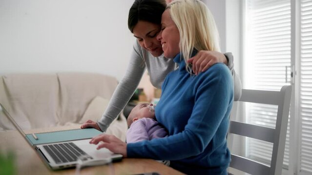 Newborn and lesbian gay mothers working with laptop computer at home - LGBTQ family, love and relationship concept