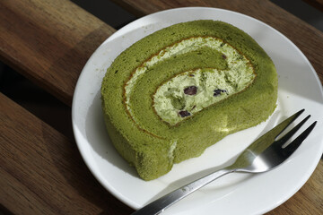 A slice of matcha roll cake on a white plate and wooden table - dark moody photography