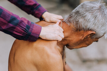 A woman, a professional doctor, makes a relaxing massage with her hands to a sick old elderly gray-haired retired man with scoliosis on his back. Photography, close-up portrait.