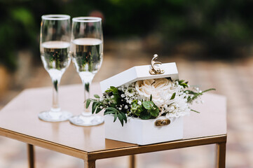 A box of flowers and glass wine glasses with champagne are on the table at the wedding ceremony....