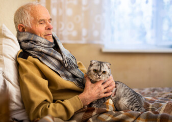 Elderly man sits on a bed with a scottish fold cat in his arms