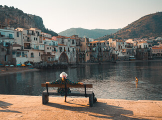 Women sitting on bench, enjoying view of beach town of Cefalu in Sicily, Italy 