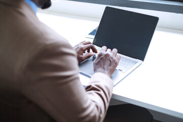 Black businessman typing on laptop keyboard in modern office. 