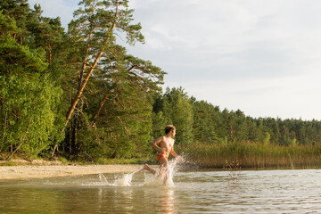 A slender guy child teenager runs along the water along the coast at sunset, splashing from the water.