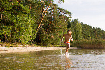 A slender guy child teenager runs along the water along the coast at sunset, splashing from the water.