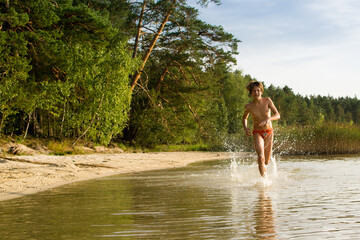 A slender guy child teenager runs along the water along the coast at sunset, splashing from the water.