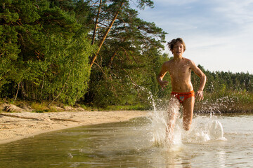 A slender guy child teenager runs along the water along the coast at sunset, splashing from the water.