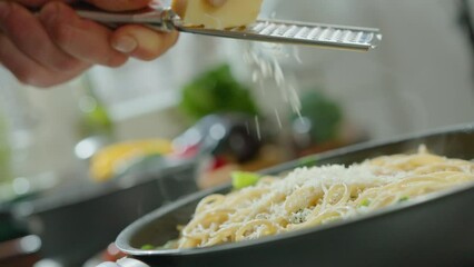 Hands of chef grating cheese over just cooked spaghetti in a frying pan, preparing Italian pasta for serving. Close-up view, dutch angle shot