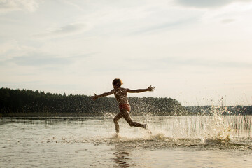 A slender guy child teenager runs along the water along the coast at sunset, splashing from the water.