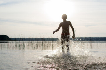 A slender guy child teenager runs along the water along the coast at sunset, splashing from the water.