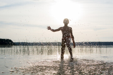 A slender guy child teenager runs along the water along the coast at sunset, splashing from the water.