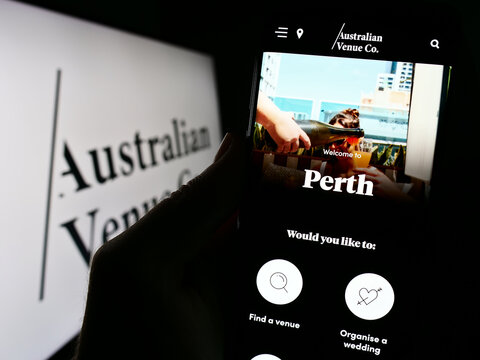 Stuttgart, Germany - 09-02-2023: Person holding cellphone with website of company Australian Venue Co. (AVC) on screen in front of logo. Focus on center of phone display.