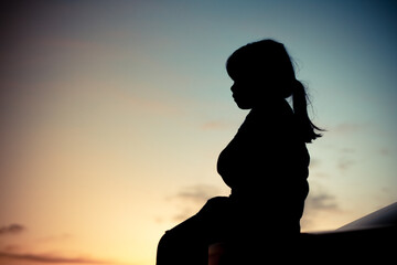 Silhouette of A girl sitting sadly in the back of the car and orange Sunset and blurred goldden and blue sky background