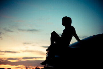 Silhouette of A girl sitting sadly in the back of the car and orange Sunset and blurred goldden and blue sky background