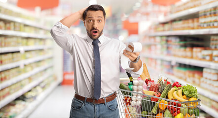 Shocked man with a bill and shopping cart holding his head in disbelief