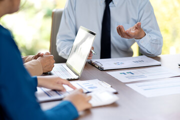 executive is pointing at a laptop to provide attendees with graphs