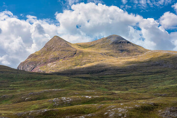 Green mountains jutting out among grassy meadows in the Highlands of Scotland, UK.