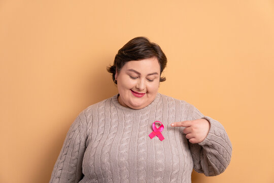 happy brazilian woman showing pink ribbon in all beige colors. breast cancer, awareness concept.