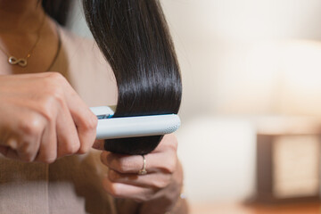 Woman with long straight hair using hair straightener with flat iron.
