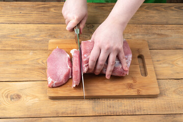 A young woman cuts raw pork meat into pieces.