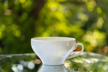 White coffee cup or mug on natural stone table against blurred green background of fresh summer greenery. Coffee time, calm, peaceful, rural way of life oudoor. Empty space for text or design