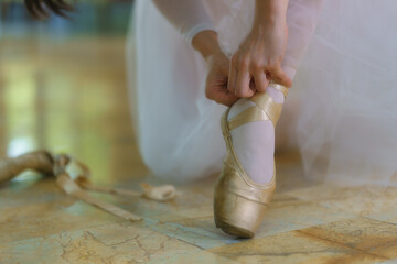 Close-up view of dancer tying ribbons of old toe shoes on the marble floor.