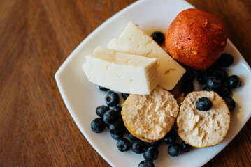 Soft cheese balls adorned with blueberries and paprika, artfully arranged on a white plate atop a rustic wooden table. Delightful culinary composition.