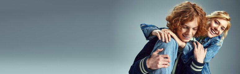 happy blonde teenage girl hugging stylish redhead boyfriend and smiling on grey, banner