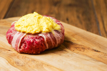 Big uncooked beef burger wrapped with bacon slice and portion of cheese on wooden board. Premium meat product. High quality cheeseburger.