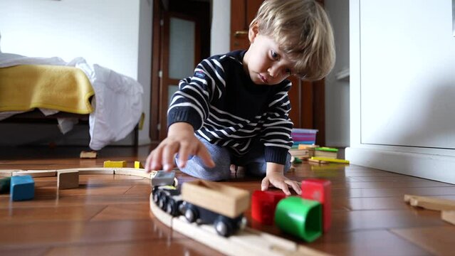 Little boy playing with vintage wooden train tracks, child immersed in imaginative play pushing retro wagon with hand
