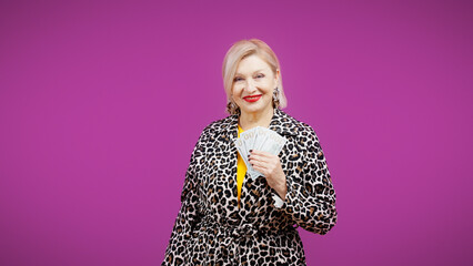 An elegant senior woman is showing money while standing against a purple background, Black Friday sales