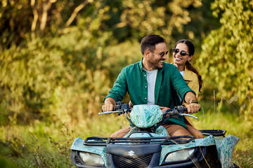 A smiling love couple enjoys the quad bike ride and looks at each other.