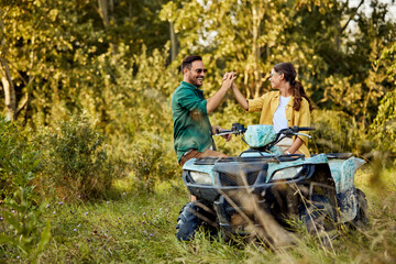 A smiling woman sitting on a quad bike gives her boyfriend a high five.